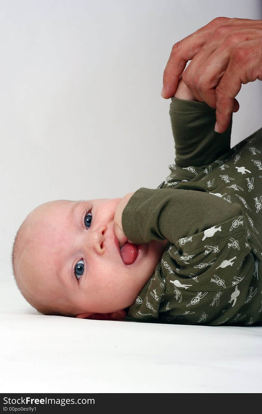 Baby on the floor with the hand of his father. The boy is putting his hand in his mouth.