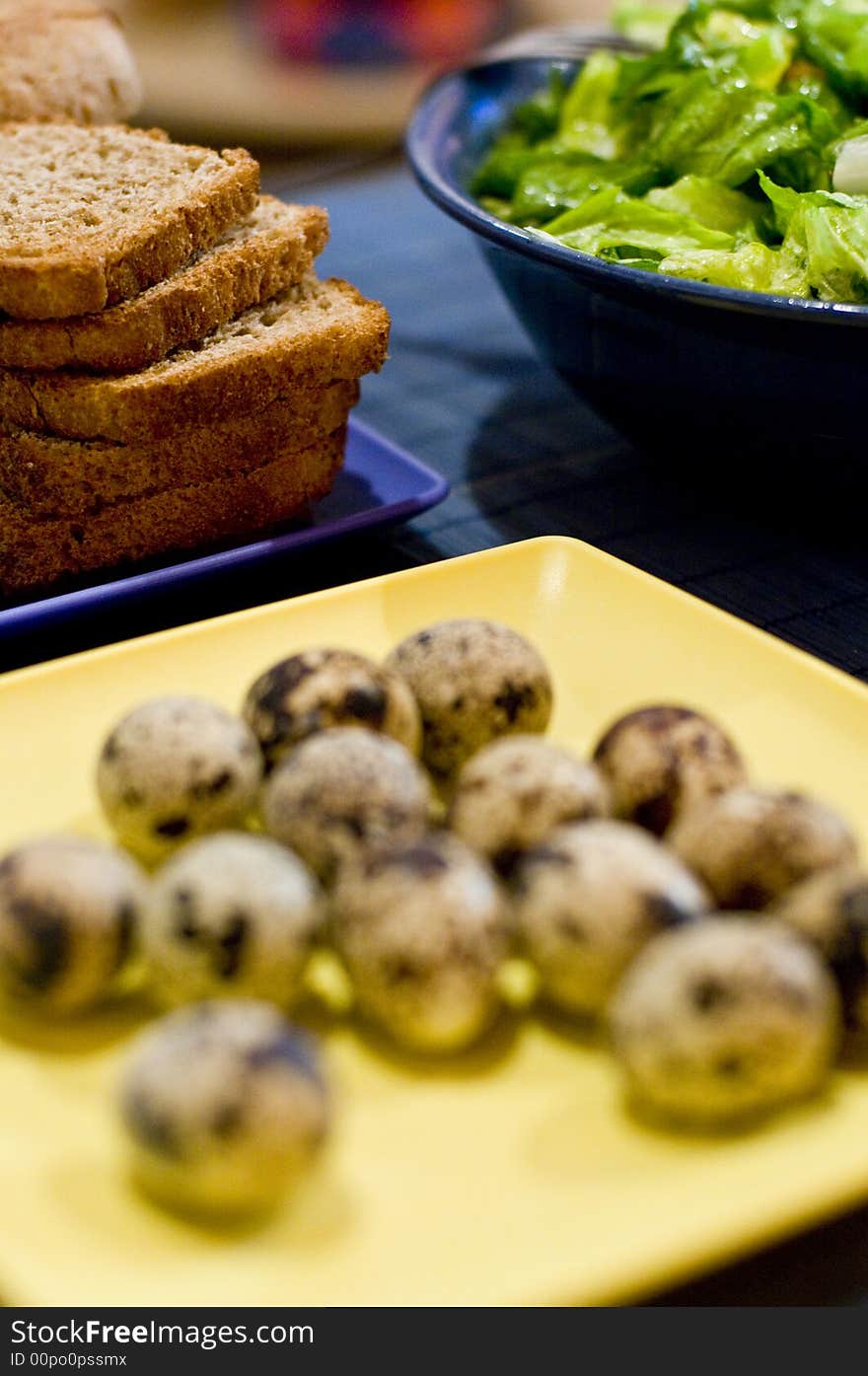 Table setting of a plate of quail eggs, slices of bread and green salad. The focus is on the background. Table setting of a plate of quail eggs, slices of bread and green salad. The focus is on the background.