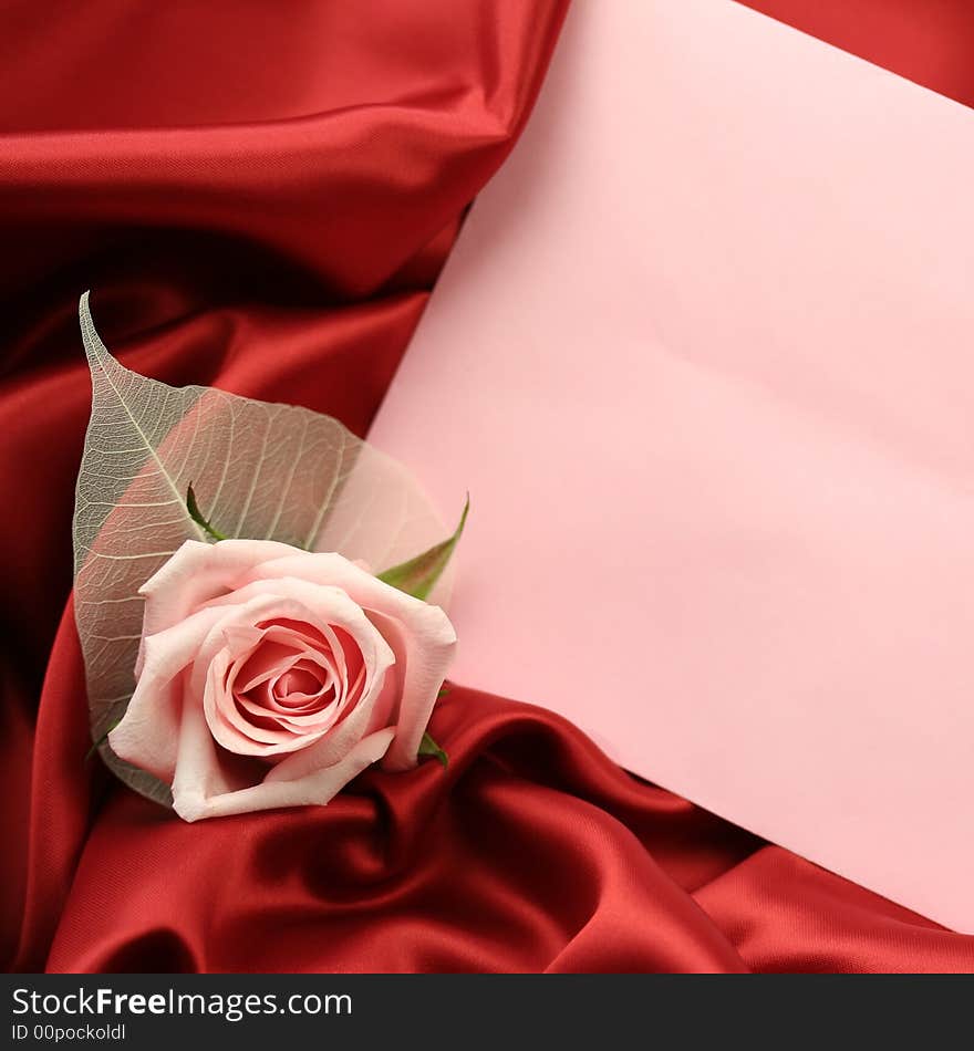 A detail of a pink rose with an empty pink card lying on dark red satin fabric. A detail of a pink rose with an empty pink card lying on dark red satin fabric.