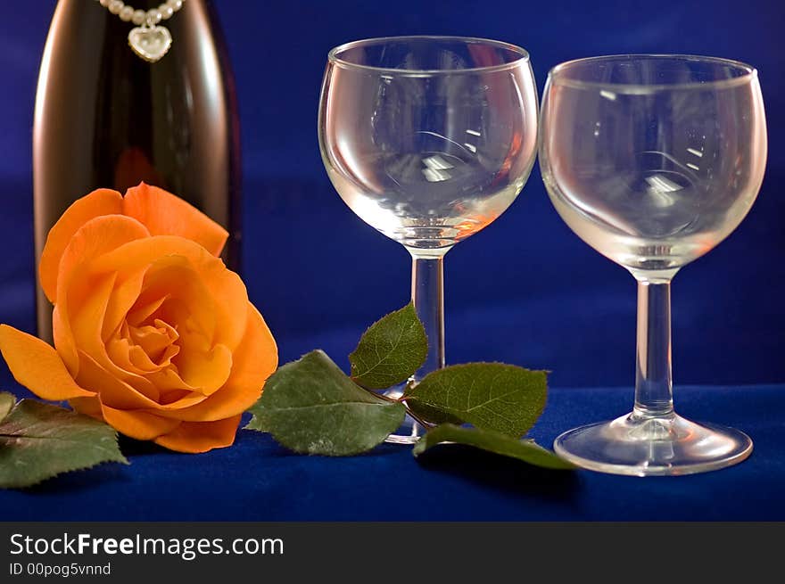 A closeup view of two empty wine glasses and a peach rose with a bottle of wine in the background. A closeup view of two empty wine glasses and a peach rose with a bottle of wine in the background.