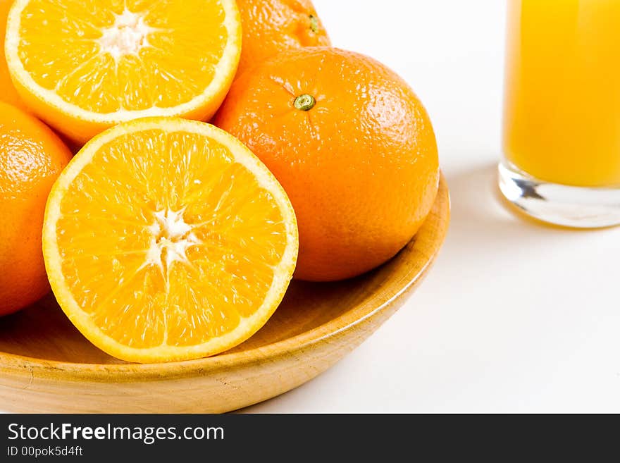 Two halves of orange in a wooden bowl with uncut oranges and a glass of orange juice in the background. Two halves of orange in a wooden bowl with uncut oranges and a glass of orange juice in the background