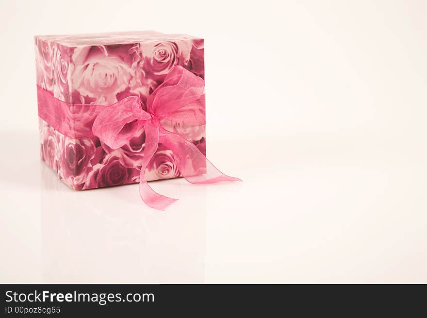 A floral patterned box lying on the side,  on a pastel pink background. It has a cerise pink ribbon around it. A floral patterned box lying on the side,  on a pastel pink background. It has a cerise pink ribbon around it.