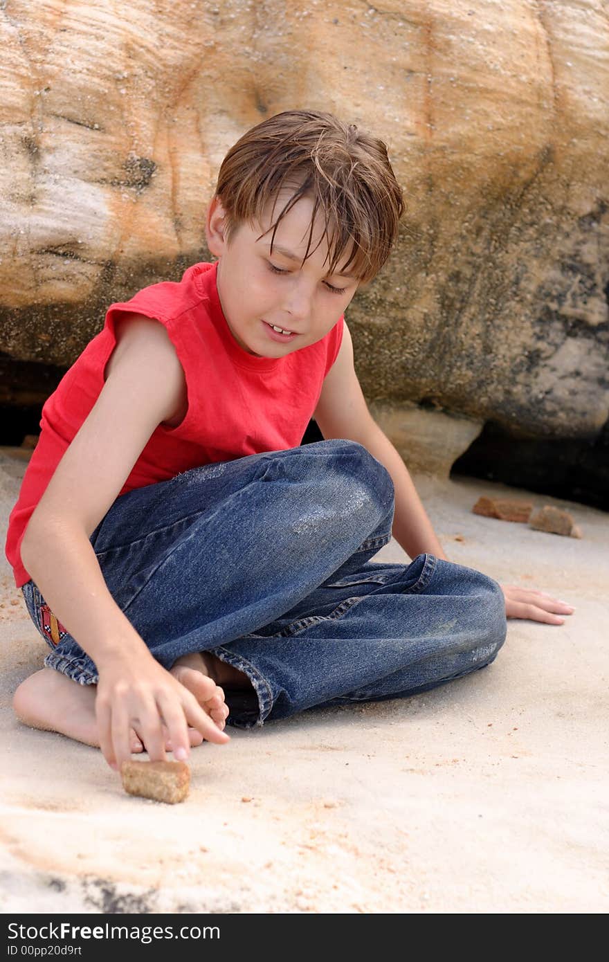A casually dressed boy amuses himself playing with stones among sandstone rocks outdoors. A casually dressed boy amuses himself playing with stones among sandstone rocks outdoors
