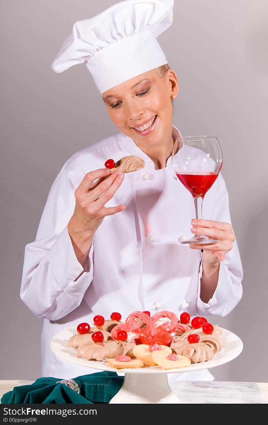 Passive posed smiling female Chef enjoying a cookie from and elegant cherry dessert plate. Passive posed smiling female Chef enjoying a cookie from and elegant cherry dessert plate.