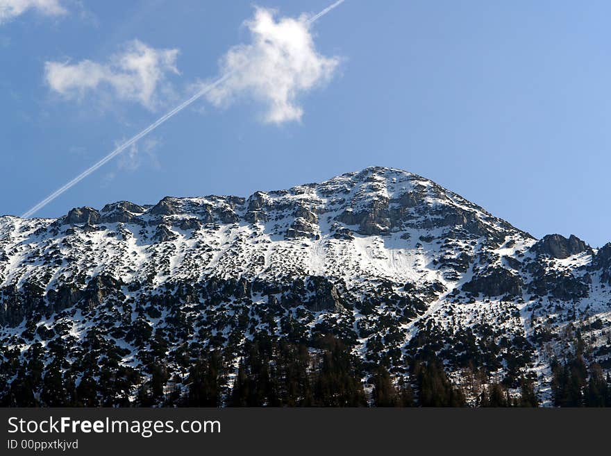 Alpes, Bavaria, Germany -Not so far from  Inzell City .Peak of Zwisel Mountain at the background of sky clouds and airplane track. Alpes, Bavaria, Germany -Not so far from  Inzell City .Peak of Zwisel Mountain at the background of sky clouds and airplane track.