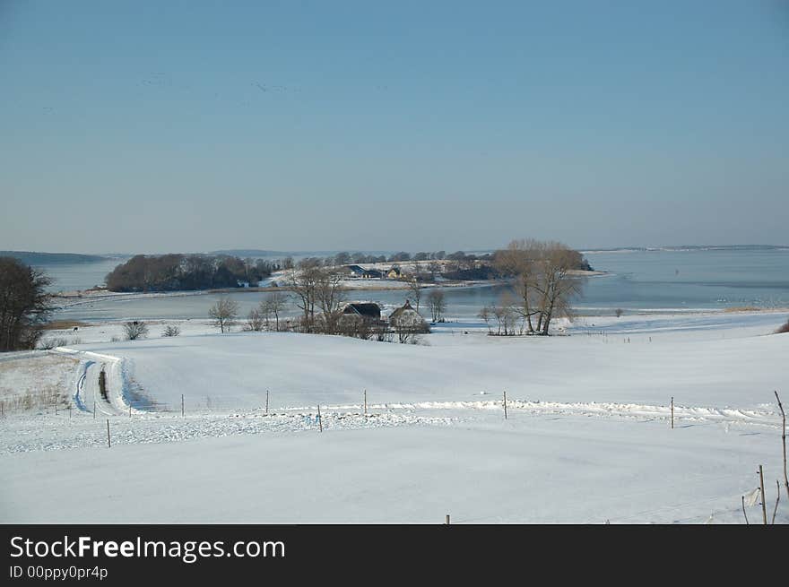 Idylic winter landscape with, fram, fields and frozen sea.