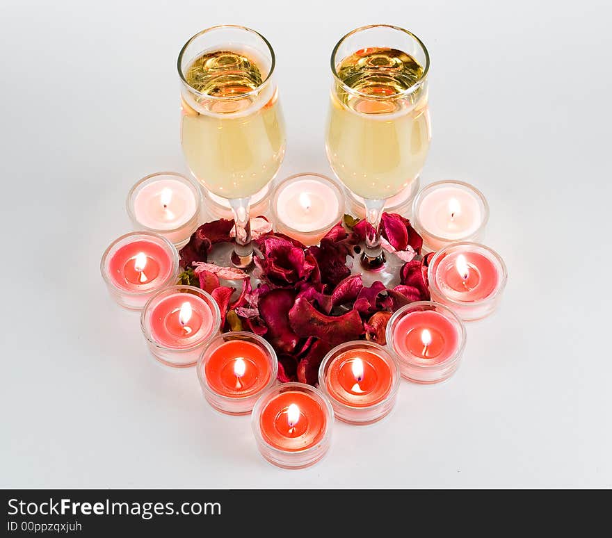 Heart from burning candles with two glasses of a champagne on white background. Valentine's day decoration.