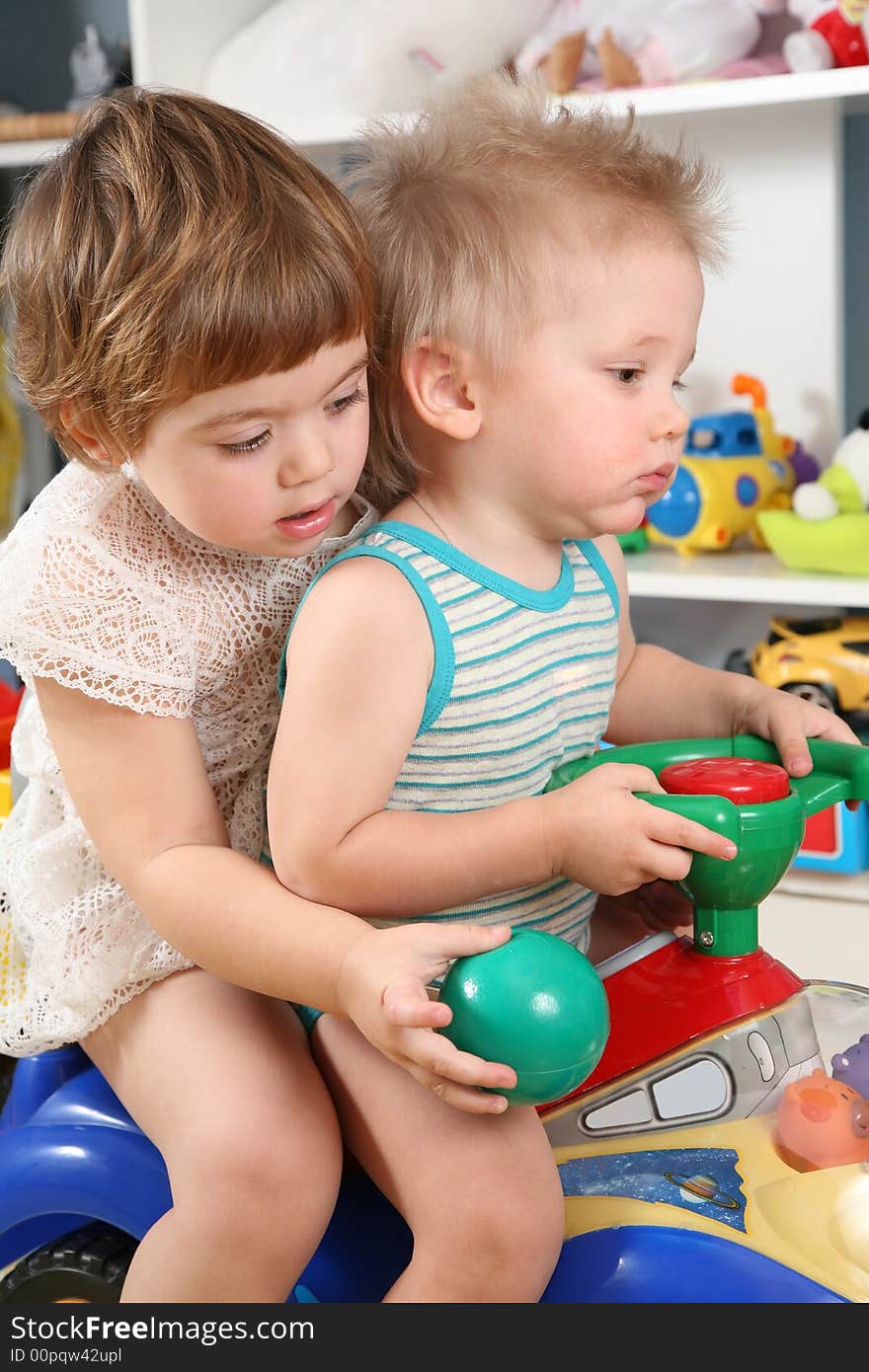 Two Children In Playroom On Toy Scooter