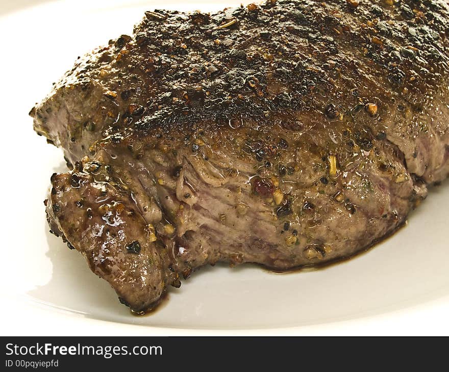 Piece of beef steak spiced with black pepper on a white plate. Piece of beef steak spiced with black pepper on a white plate