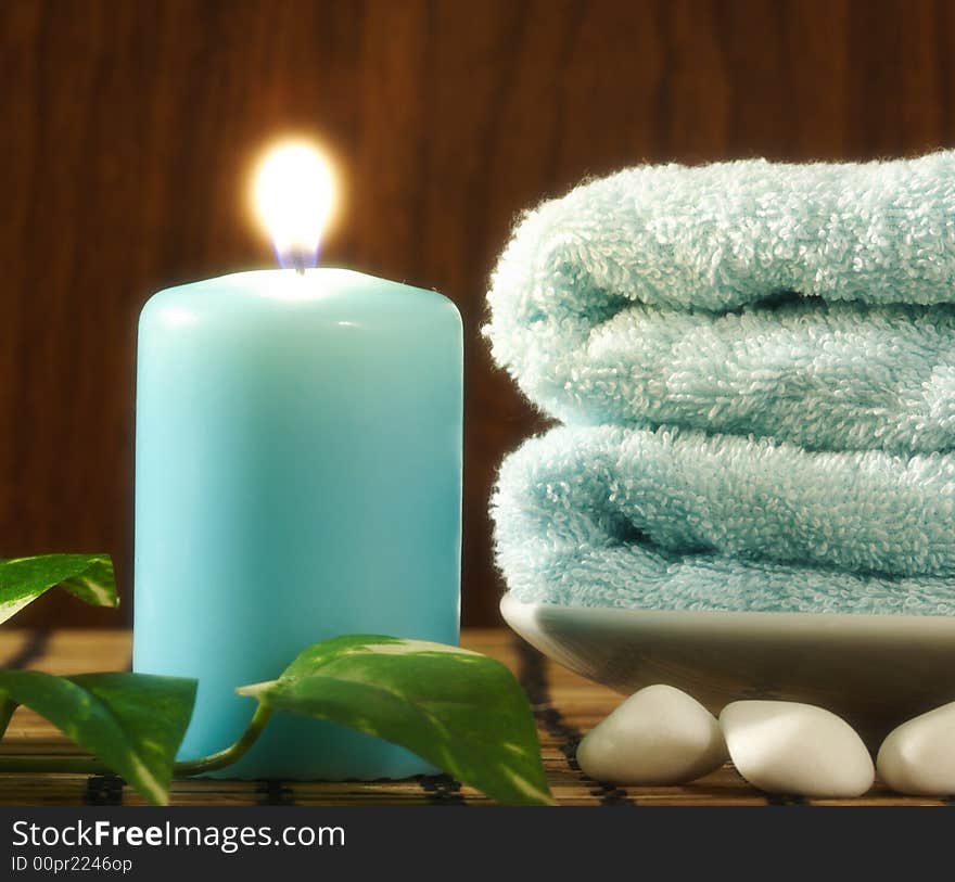 Blue towel and candle, green leaf and a few white stones in front of wood background. Blue towel and candle, green leaf and a few white stones in front of wood background