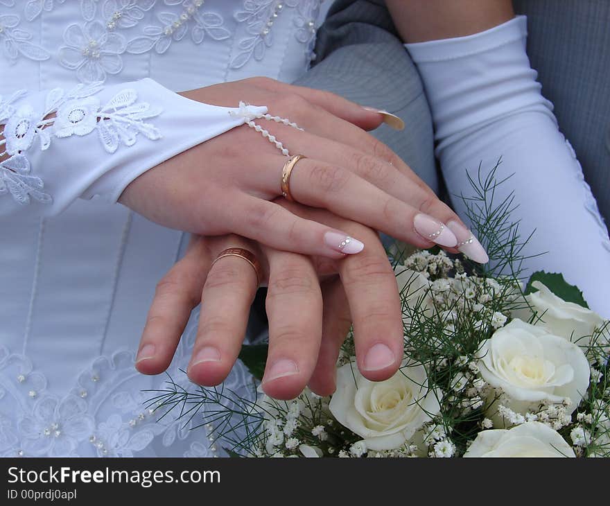 Hand of the groom and the bride with wedding rings and a bouquet of white roses. Hand of the groom and the bride with wedding rings and a bouquet of white roses