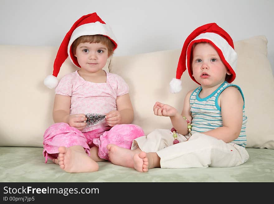 Two children on sofa in santa claus hats. Two children on sofa in santa claus hats