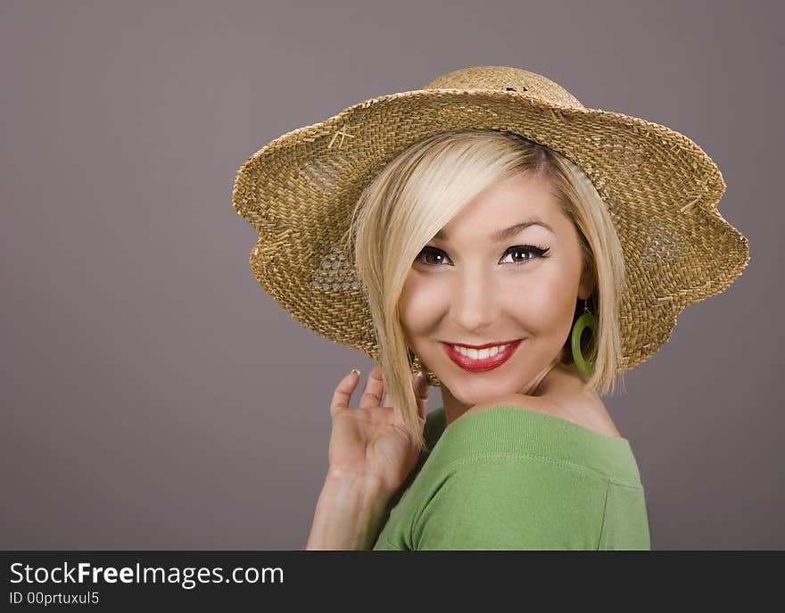 A blonde model in a green blouse and a straw hat smiling at the camera. A blonde model in a green blouse and a straw hat smiling at the camera