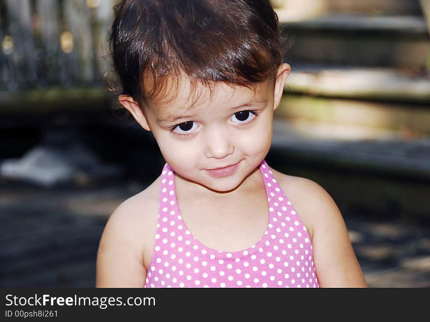 Cute little baby girl giving a look of sweetness wearing a pink polka dot halter dress.  She has big brown eyes and brunette hair with a redish tint.