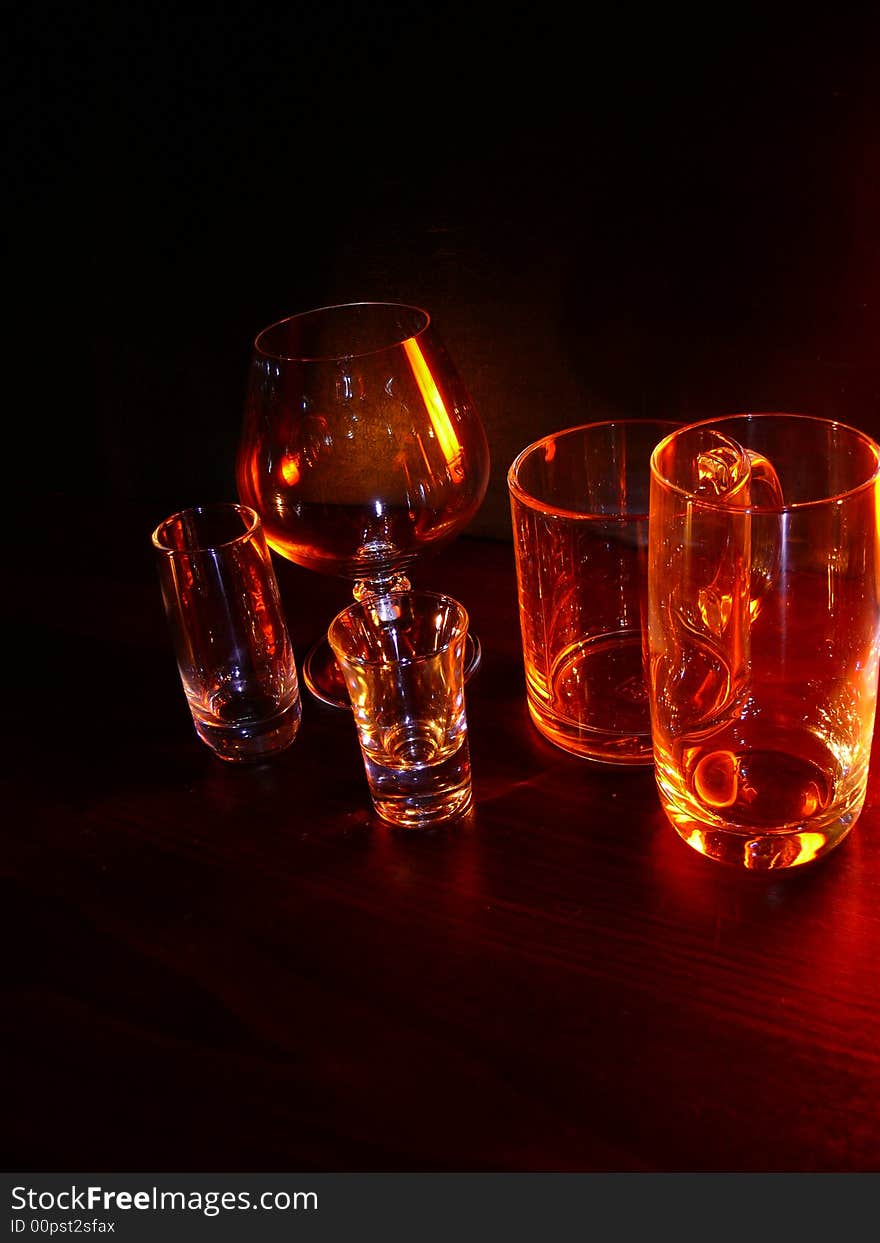 Glasses, wineglasses and a cup on a black background, specks of light, evening light