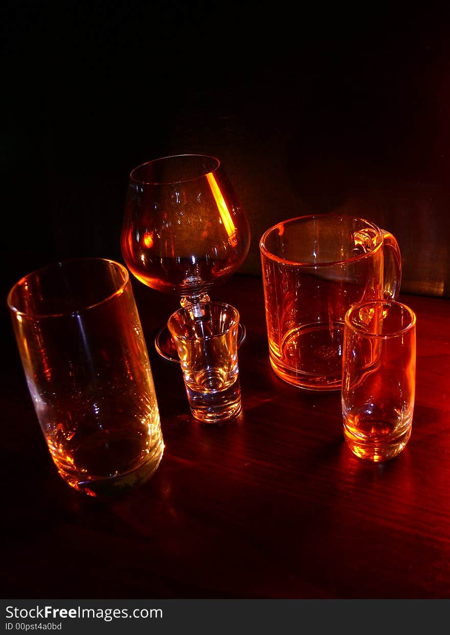 Glasses, wineglasses and a cup on a black background, specks of light, evening light