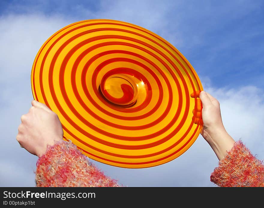 Red the and orange disc in the girl's palms on background of blue sky. Red the and orange disc in the girl's palms on background of blue sky