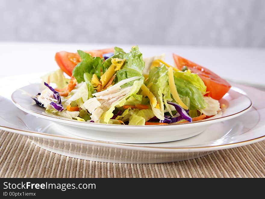 Healthy salad with lettuce, carrots, radish, cabbage, turkey, tomato wedges, and cheese