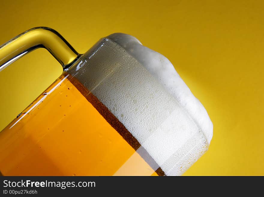 Beer mug with froth close-up over yellow background