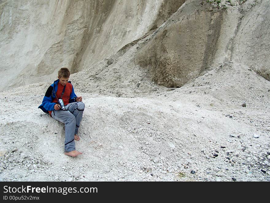 The teenager with a camera, sitting on a beach near a rock from limestone. The teenager with a camera, sitting on a beach near a rock from limestone