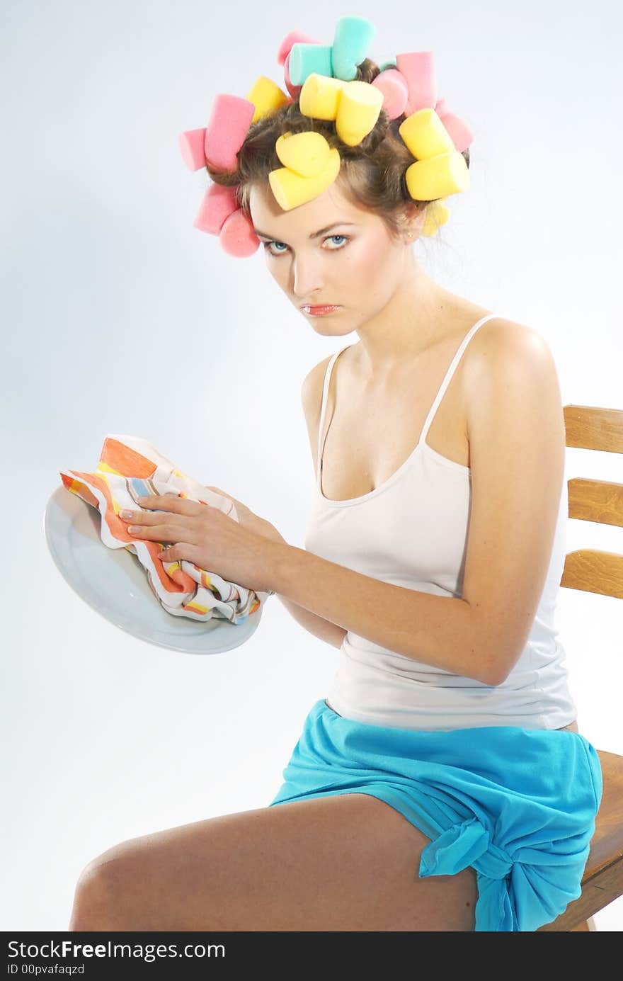 A woman in hair curlers is drying up the plate. A woman in hair curlers is drying up the plate