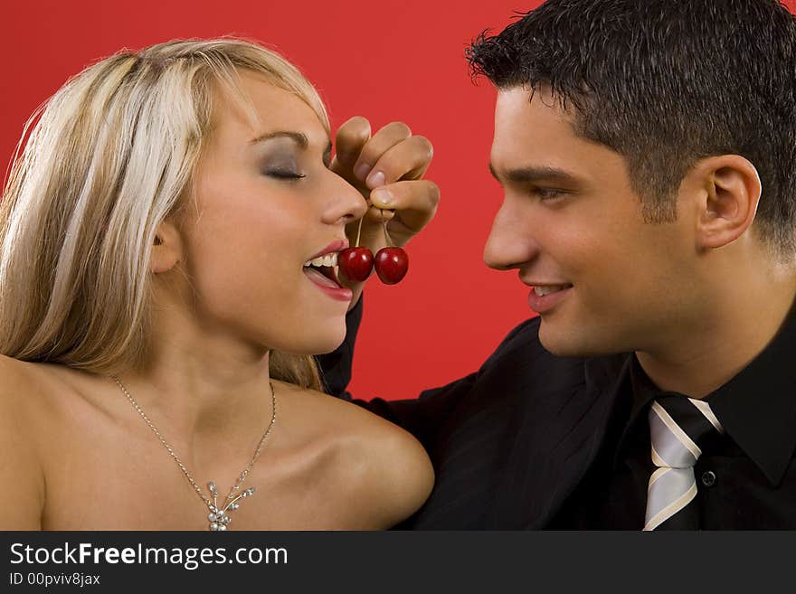 Young enamoured couple. Man is feeding woman by cherry and smiling. Young enamoured couple. Man is feeding woman by cherry and smiling