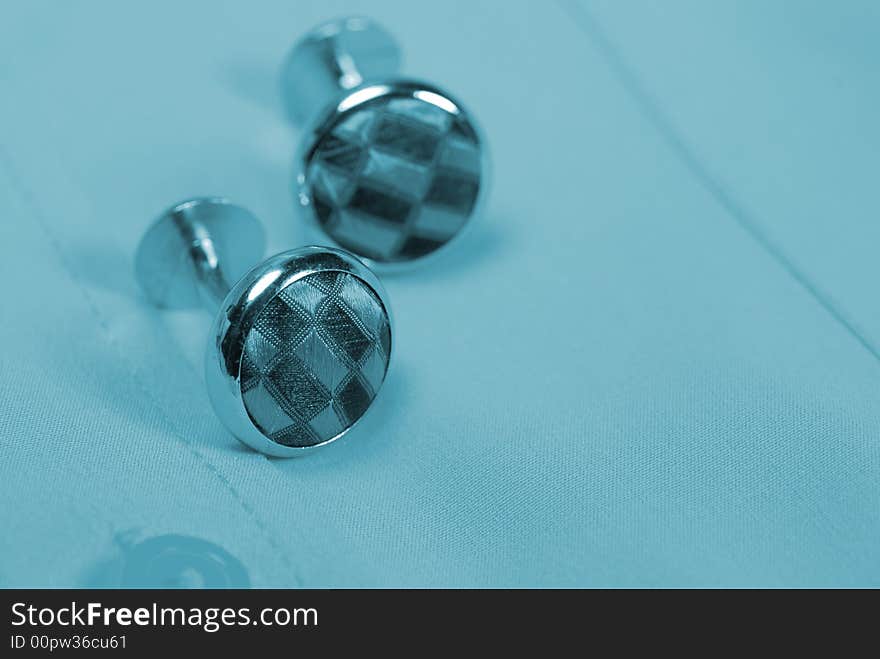 Pair of cuff links on a shirt with a blue tint. Pair of cuff links on a shirt with a blue tint