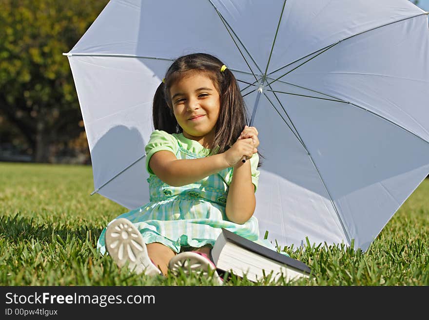 Little girl playing with a white umbrella and book on the ground. Little girl playing with a white umbrella and book on the ground