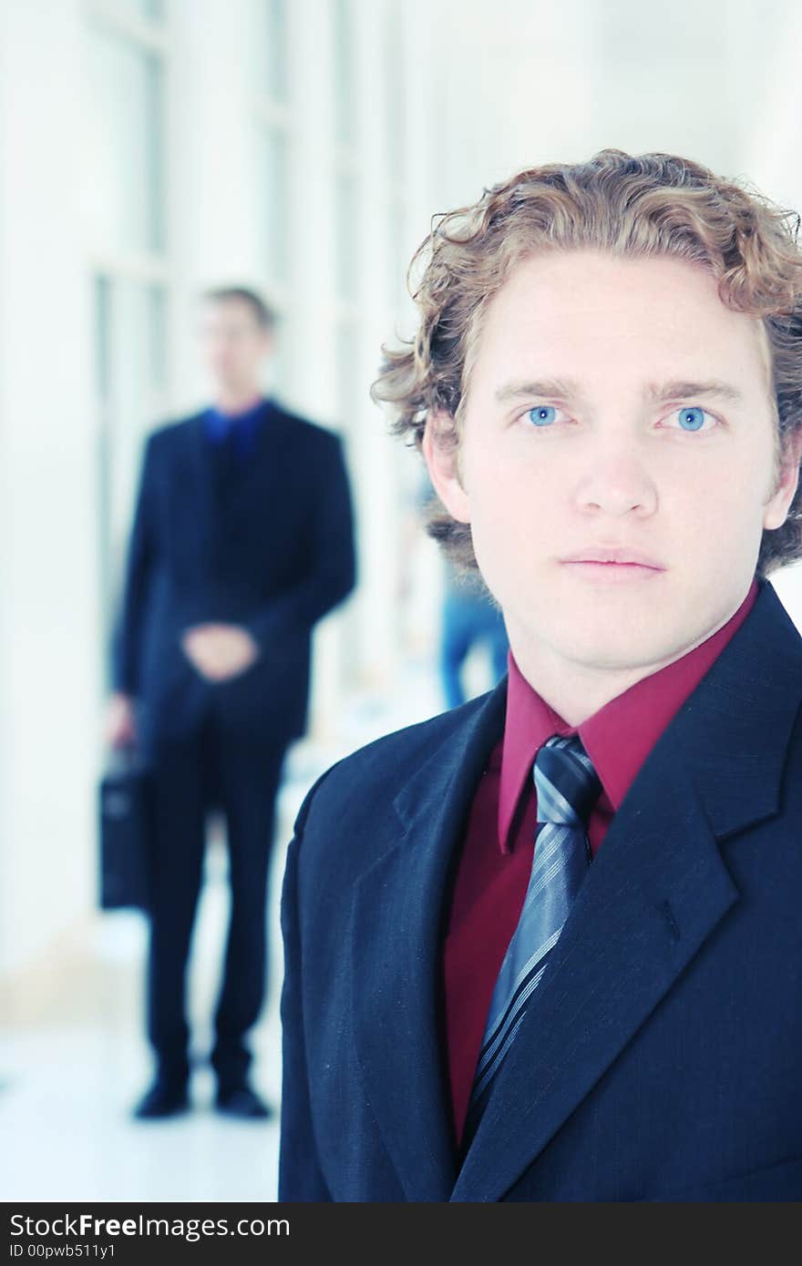 Two businessmen in hallway, one with a briefcase, the other with very blue eyes