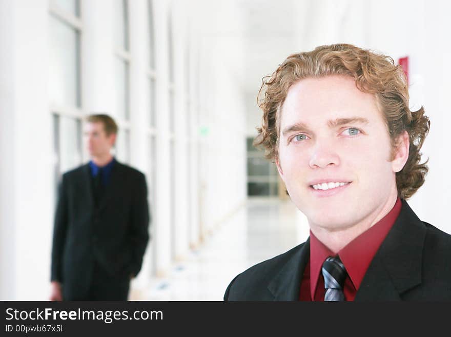 Two businessmen in hallway, one pauses to smile