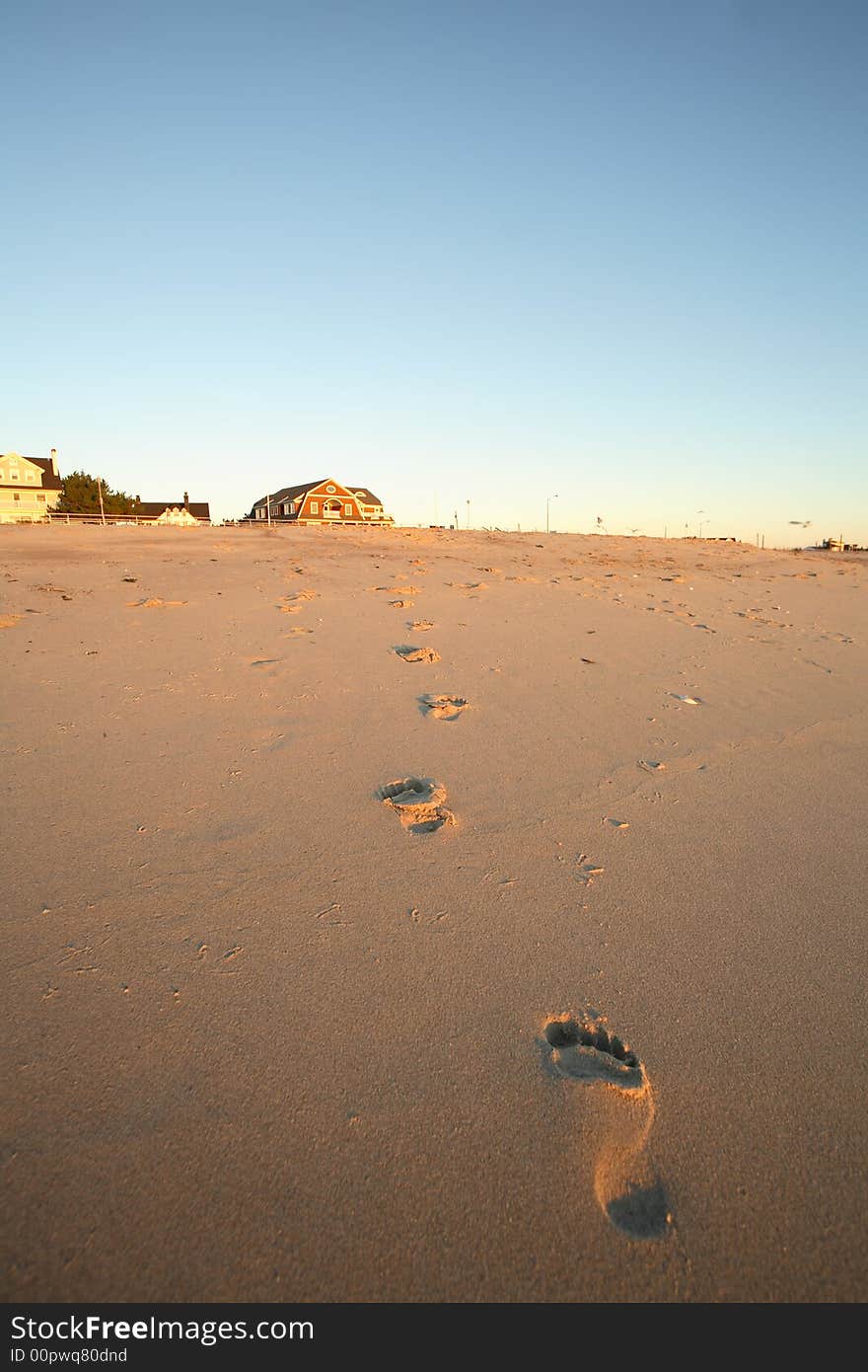 Barefoot prints on the beach leading to a distant beach house in this idyllic vacation image. Barefoot prints on the beach leading to a distant beach house in this idyllic vacation image.