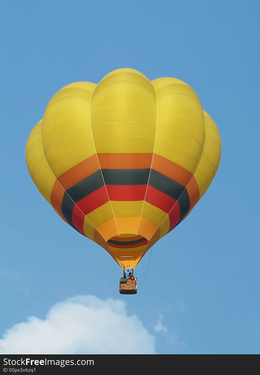 Yellow hot-air balloon flying mid-air. Blue sky background.