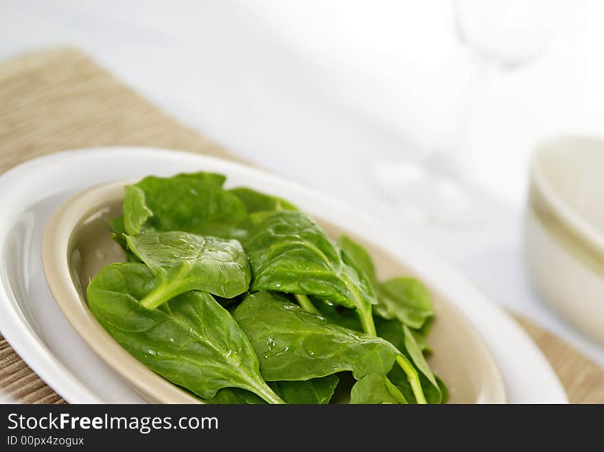 Fresh raw spinach leaves on a plate with placemat. Low DOF.