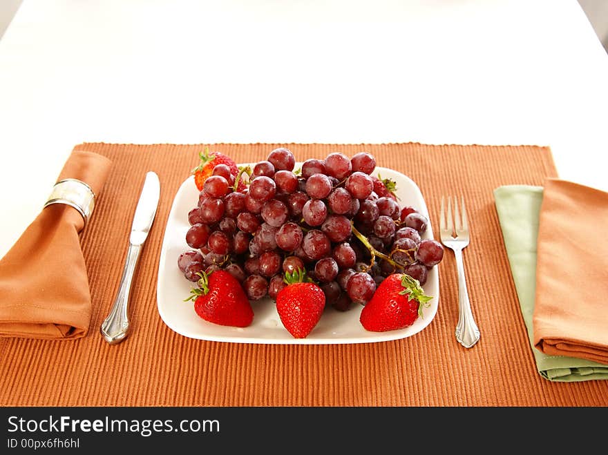 Concept: Eat more fruit. Plate piled high with red grapes, accented with strawberries, napkins, fork, and table accessories. Concept: Eat more fruit. Plate piled high with red grapes, accented with strawberries, napkins, fork, and table accessories.