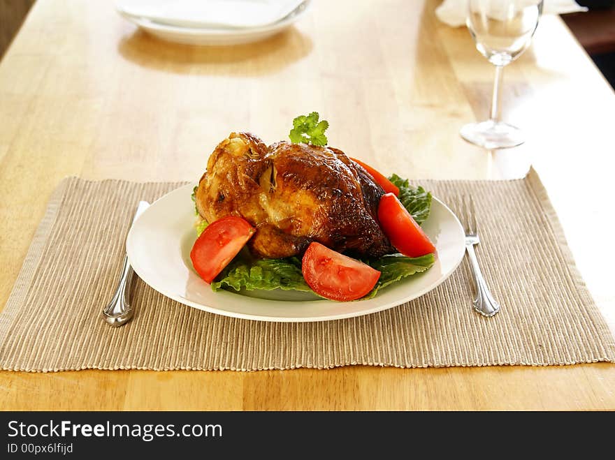 Whole roasted chicken on bed of lettuce with tomatoe wedges.