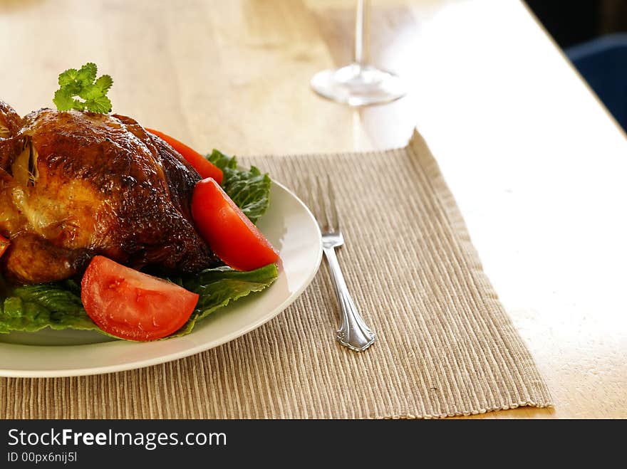 Whole roasted chicken on bed of lettuce with tomatoe wedges.