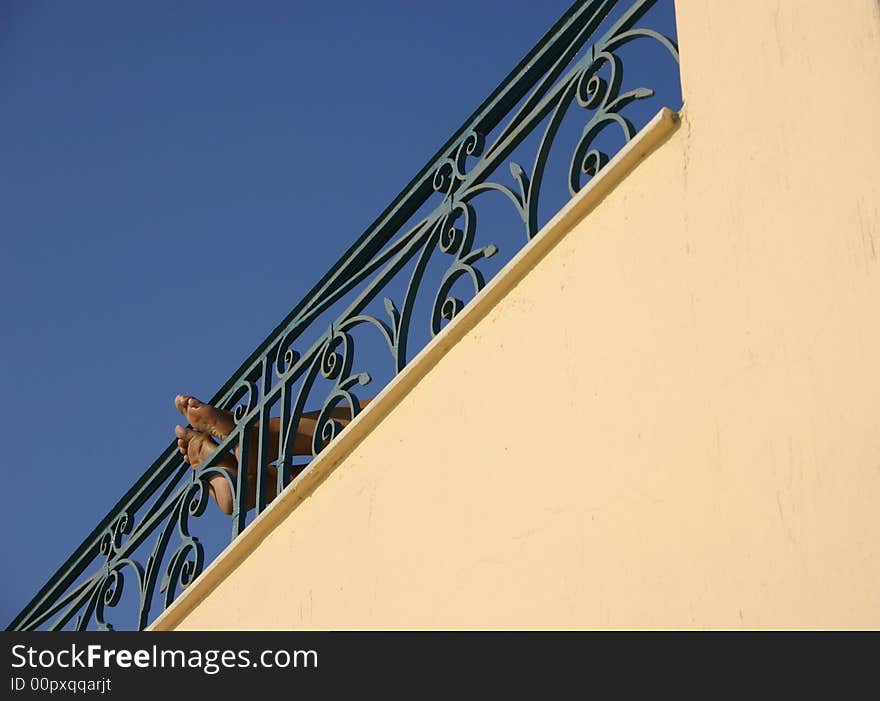 Feet resting on wrought iron railing beneath a blue sky suggesting relaxation. Feet resting on wrought iron railing beneath a blue sky suggesting relaxation