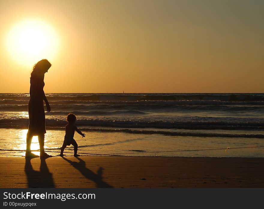 Young woman with small child on the sea shore on sunset