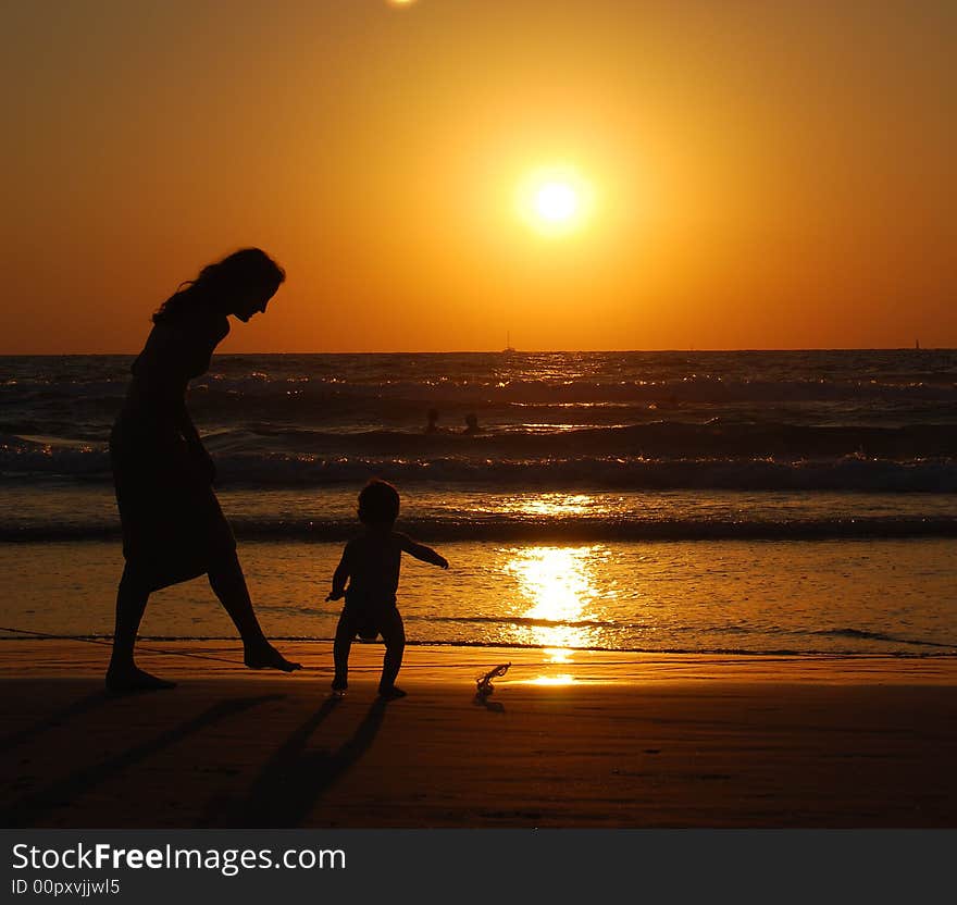 Young woman with small child on the sea shore on sunset