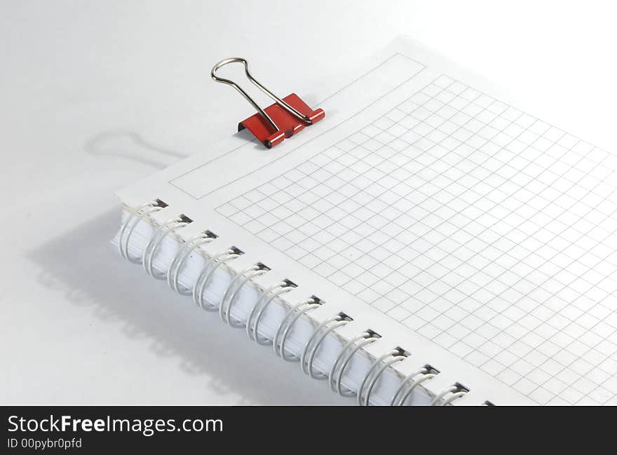 White notebook and red paperclip on white surface