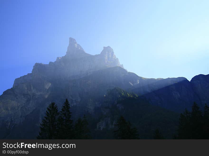 Sunlight streams over two alpine peaks. Sunlight streams over two alpine peaks