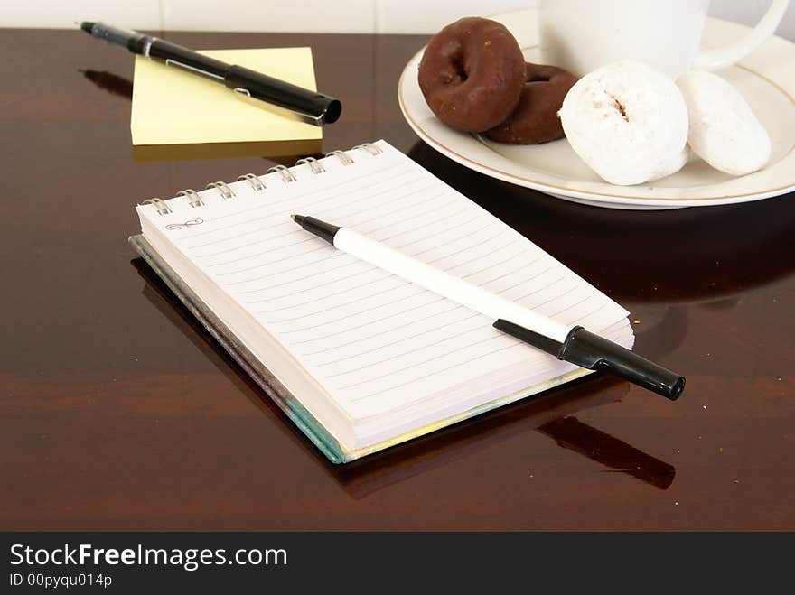 Office desk with notepads, pens, coffee and doughnuts. Office desk with notepads, pens, coffee and doughnuts