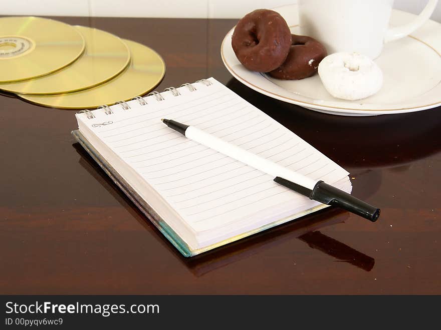 Office desk with notepad, pen, coffee, doughnuts and CDs. Office desk with notepad, pen, coffee, doughnuts and CDs