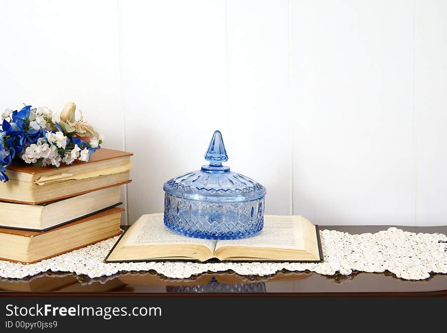 Home decor arrangement with books, crystal dish, silk flowers and antique doily.