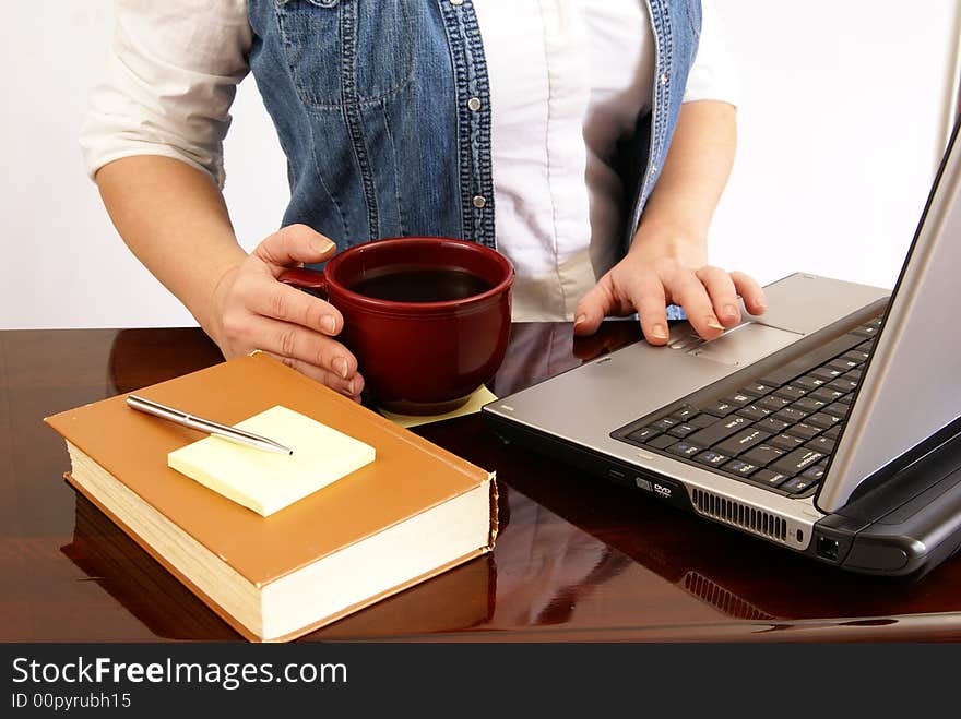 Woman working at a laptop on desk with book, pen, paper, and coffee. Woman working at a laptop on desk with book, pen, paper, and coffee.