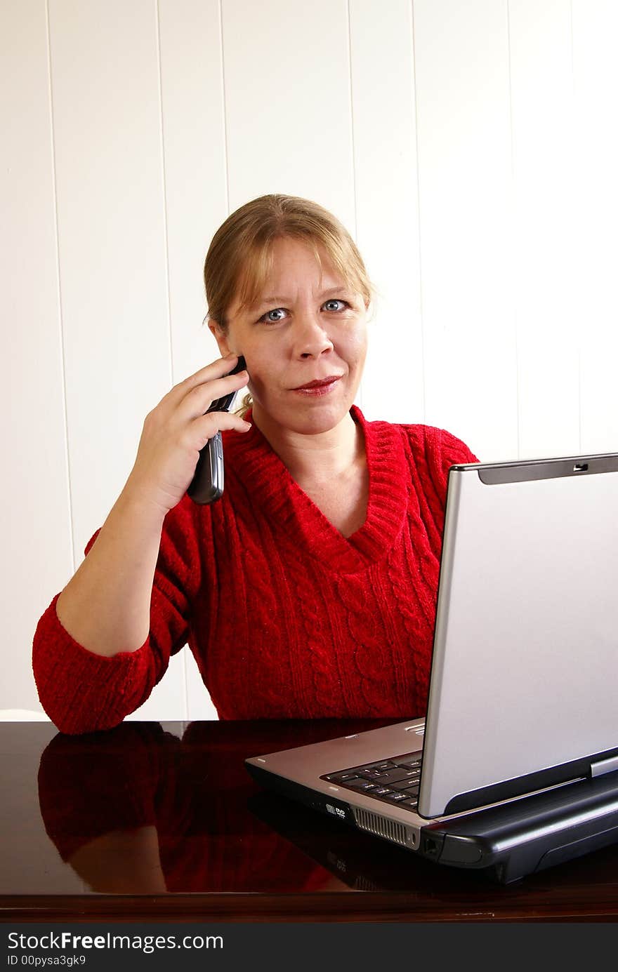 Woman in red sweater working at a laptop computer while talking on cell phone. Woman in red sweater working at a laptop computer while talking on cell phone