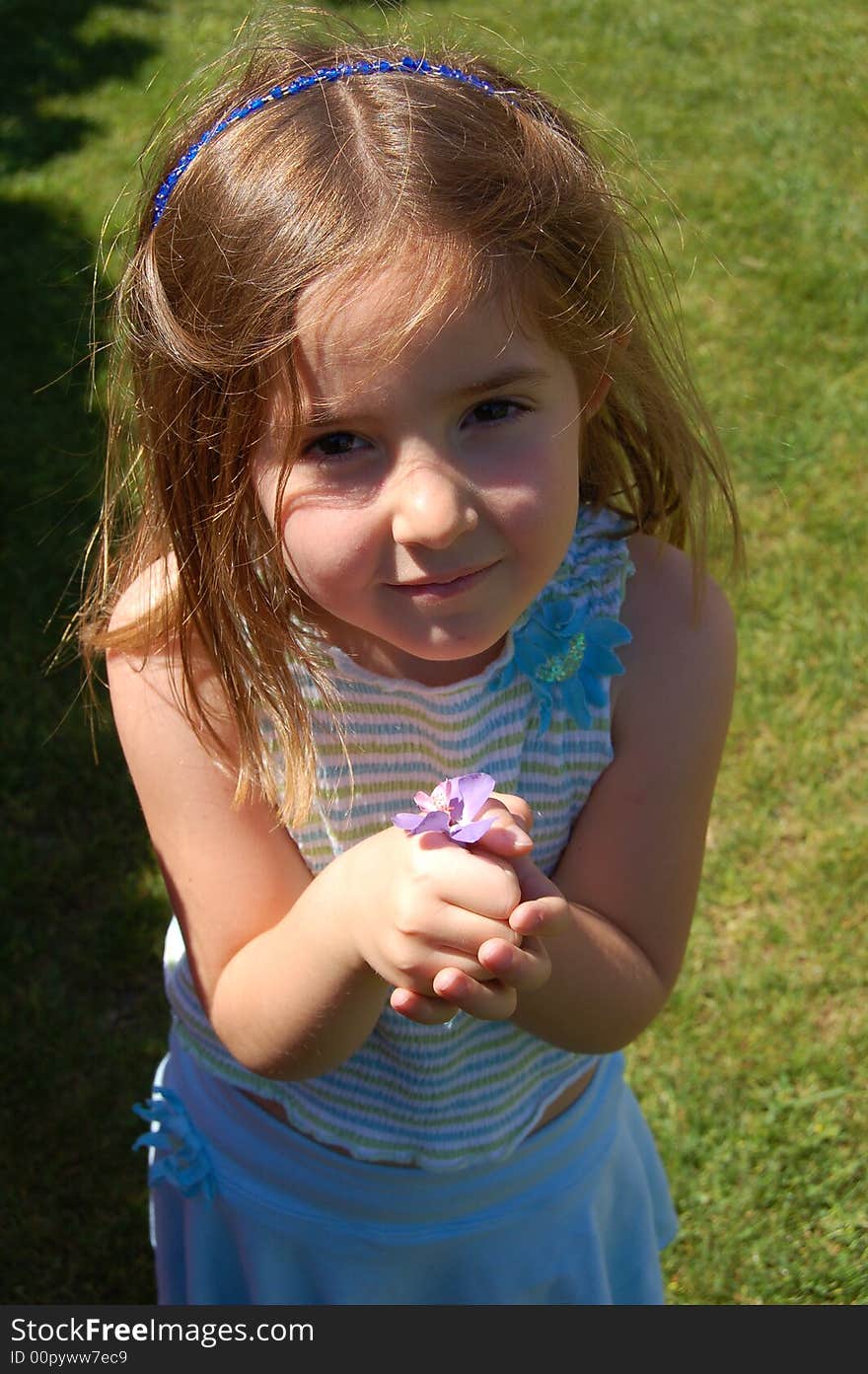 Little girl stands in the grass wearing spring colors holding flowers. Little girl stands in the grass wearing spring colors holding flowers