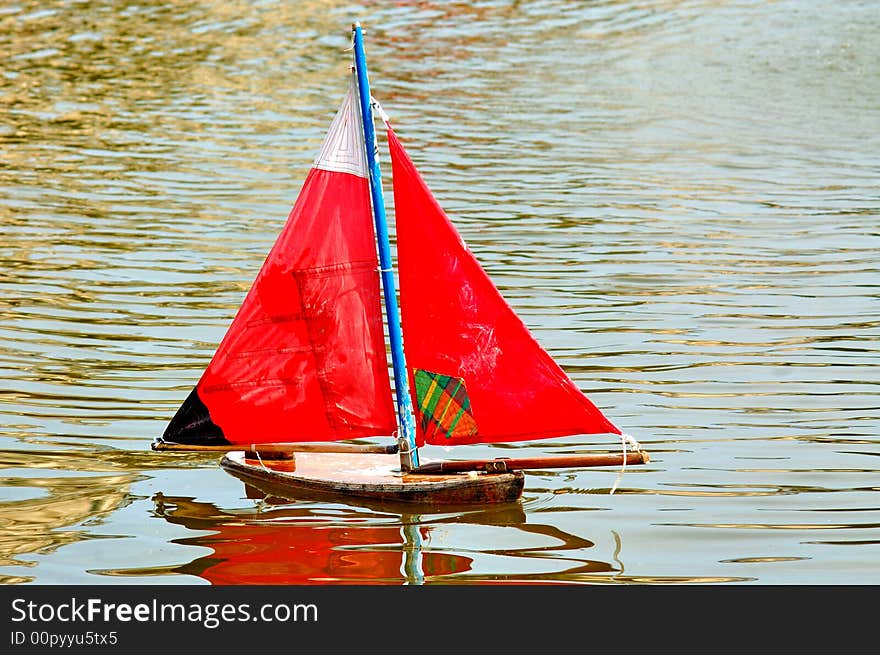 France, Paris: green water yellow leaves and a little toy boat with red sail. France, Paris: green water yellow leaves and a little toy boat with red sail