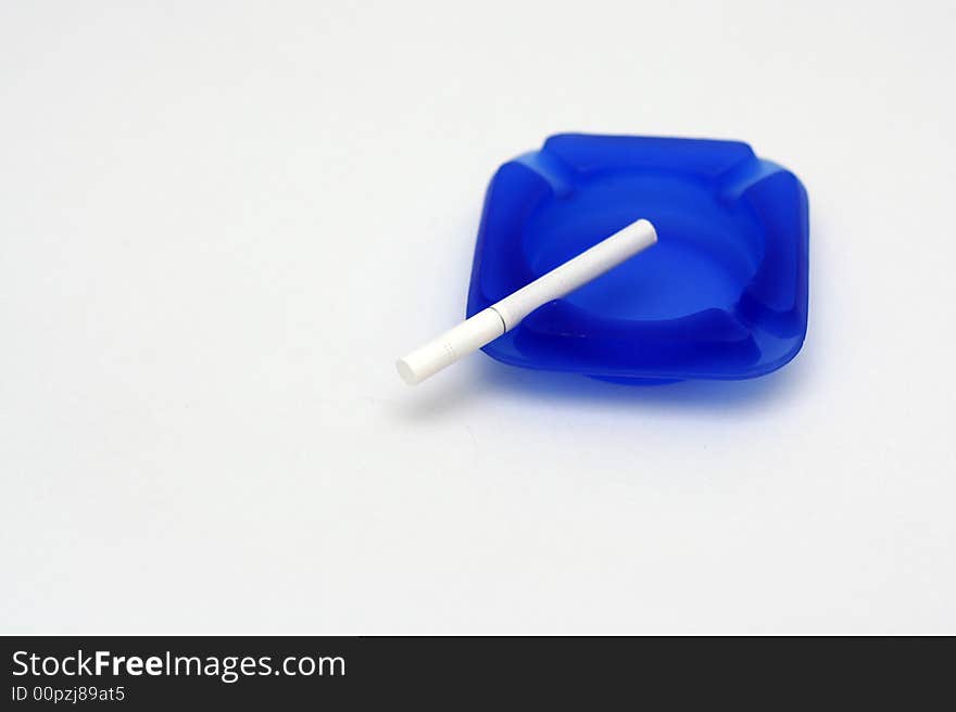 White cigarette on blue ashtray with white background. White cigarette on blue ashtray with white background