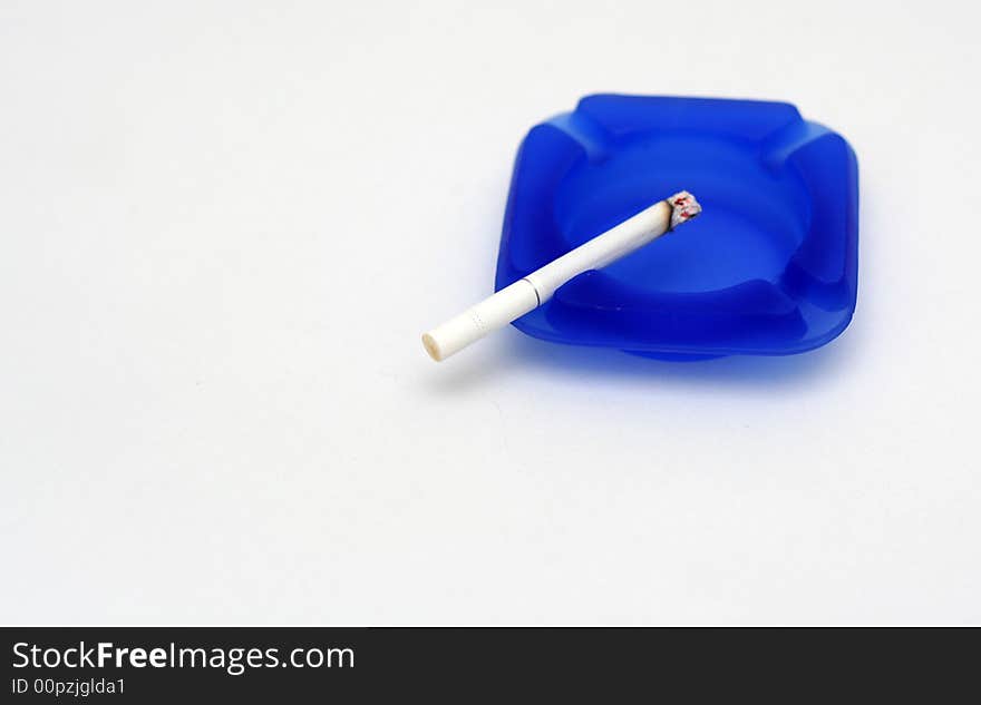 White cigarette on blue ashtray with white background. White cigarette on blue ashtray with white background